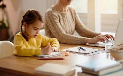 Little girl doing homework while mother is working on a computer at home.