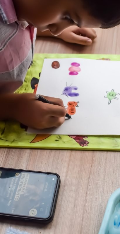 Smart Indian little boy perform thumb painting with different colourful water colour kit during the summer vacations, Cute Indian Kid doing colourful thumb painting drawing on wooden table