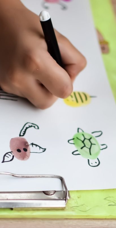 Smart Indian little boy perform thumb painting with different colourful water colour kit during the summer vacations, Cute Indian Kid doing colourful thumb painting drawing on wooden table